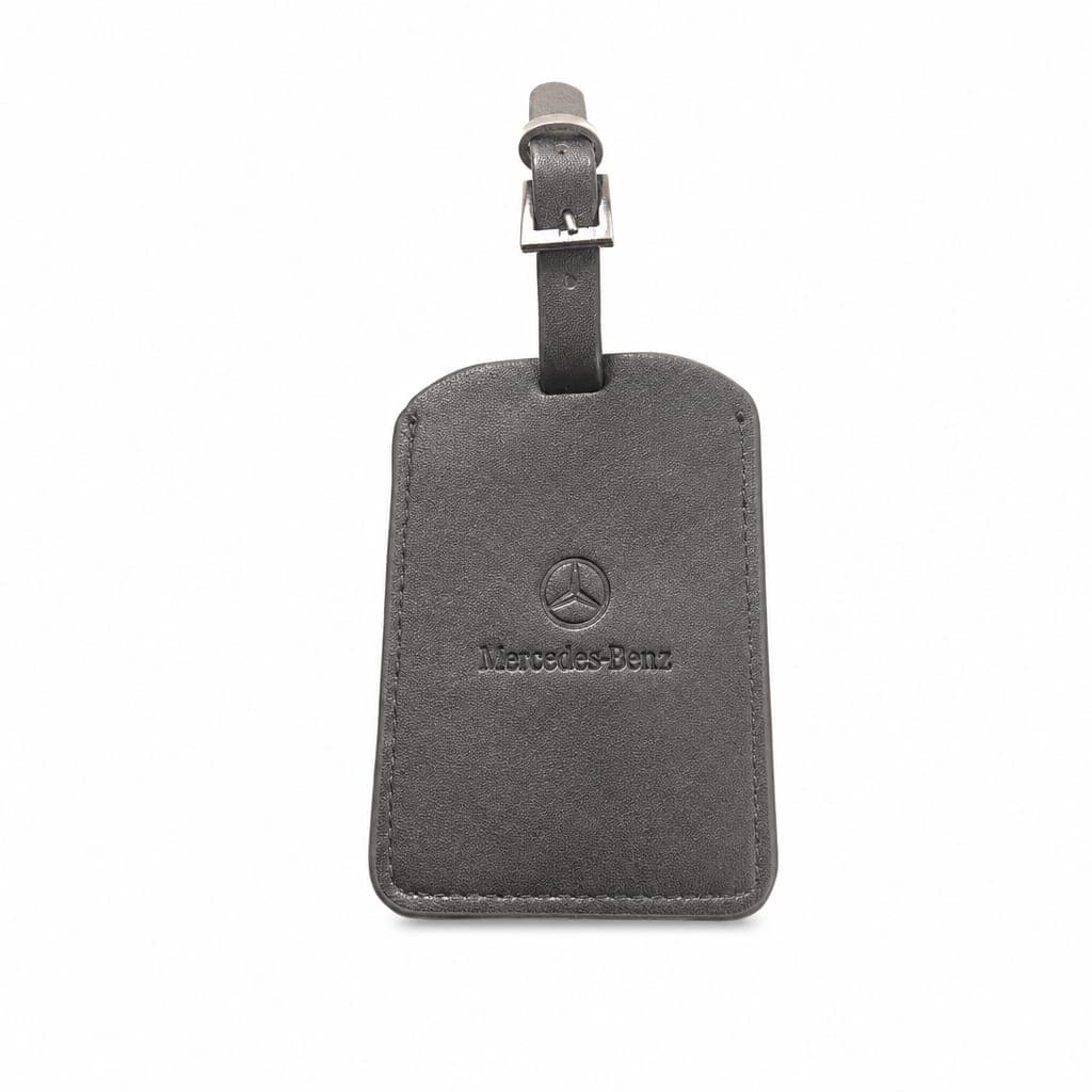 Charcoal-leather luggage tag with the three-pointed star and Mercedes-Benz word-mark debossed below it, finished with a polished steel buckle and stitched edge — designed and made by Sense2 for Mercedes-Benz.